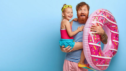 Image of happy redhaired father and daughter have glad expressions, pose with swimming equipment,...