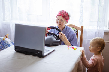 Senior woman enjoying car racing video game on laptop while her great granddaughter watching her play