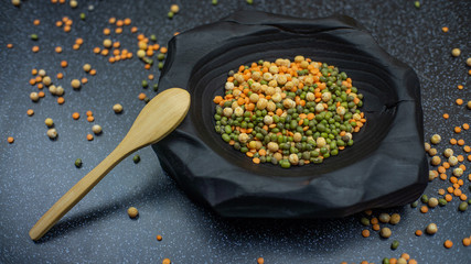 Legumes Lentils, peas and mung beans in a black wooden bowl with a wooden spoon