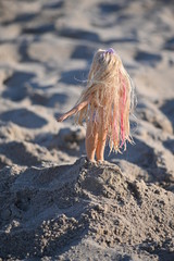 A doll with long blond hair stucks in a sand hill.