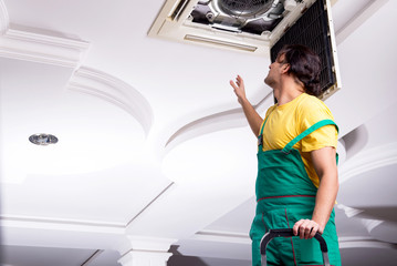 Young repairman repairing ceiling air conditioning unit