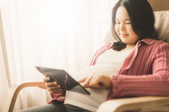 Pregnant woman feeling happy at home while taking care of her child. The young expecting mother holding baby in pregnant belly. Maternity prenatal care and woman pregnancy concept.
