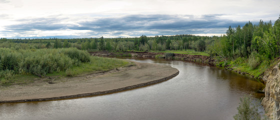 Panorama turn wild little kempendyay river in the North of Yakutia with cliffs of clay and spruce forest and a sandy flat beach.