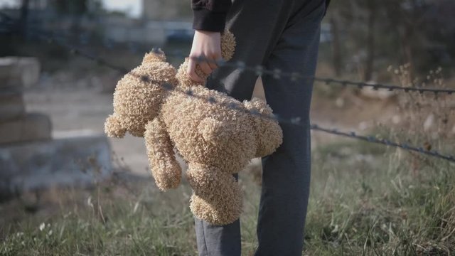 Homeless child. Homeless lonely child with a toy bear. A child with a toy behind a barbed wire. Homeless child.