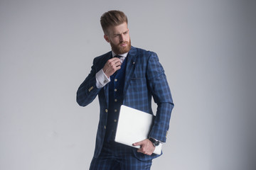 Confident business expert. Confident young handsome man in three piece suit holding laptop and smiling while standing against white background
