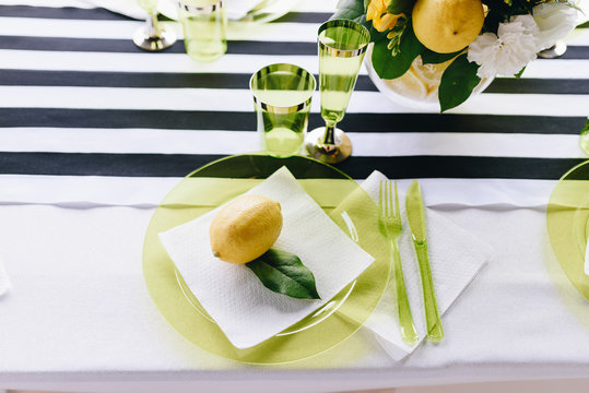A top-down whole lemon on a white napkin in a light green glass plate on a stripy tablecloth