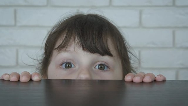 Little watcher. A cute little girl looks out from under the table.