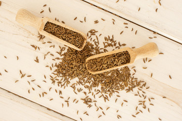 Lot of whole dry caraway fruits with two wooden scoops flatlay on white wood
