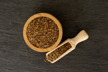 Lot of whole dry caraway fruits in a wooden bowl with wooden scoop flatlay on grey stone