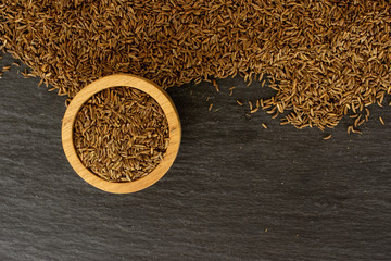 Lot of whole dry caraway fruits copyspace below in a wooden bowl flatlay on grey stone