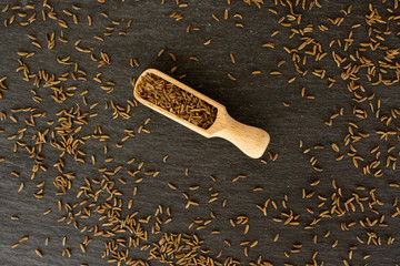 Lot of whole dry caraway fruits with wooden scoop flatlay on grey stone