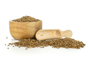 Lot of whole small dry caraway fruits in a wooden bowl with wooden scoop isolated on white...