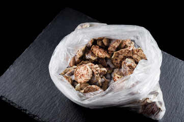 frozen dried zucchini in a plastic bag on a stone stand on a black background, isolate