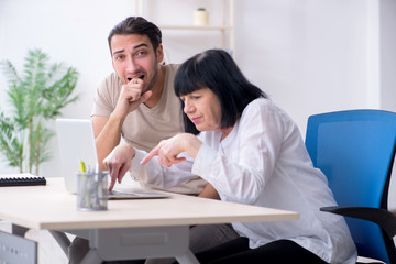 Fototapeta premium Young male employee explaining to old female colleague how to us