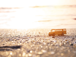 Naklejka premium Close up yellow school bus toy on sand at sunset beach.