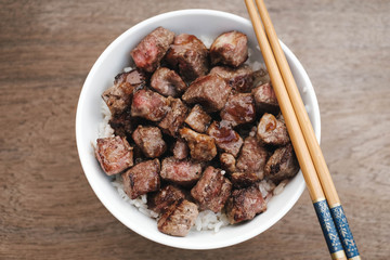 Homemade Bowl of Diced Beef Steak with rice Japanese style on wooden table.