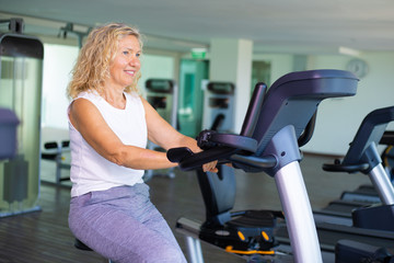 Fototapeta na wymiar Happy senior woman exercising on bike in gym.