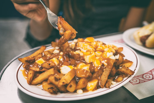 Poutine french fries canadian local classic dish in the province of Quebec, Canada. Fast food retro diner restaurant serving plate of fried potates with brown gravy sauce and fresh cheese curds.