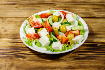 Greek salad with fresh vegetables, feta cheese and green olives on wooden table