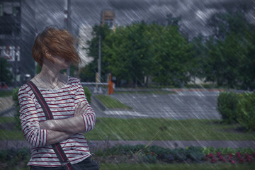 Fototapeta premium A red-haired, informally dressed middle-aged woman with freckles stands in a strong wind in the rain with her face covered by hair