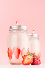 Gentle strawberry yogurts in two jars decorated sliced ripe berries with silver lids and red striped straws on soft pastel pink background, closeup, vertical.