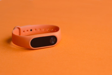 Orange fitness tracker on an orange background close up.