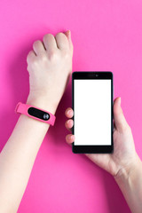 Fitness tracker on a womans hand and smartphone on pink background.