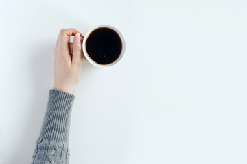 Woman hands in a gray sweater hold a cup of black coffee. Top view with place for text.