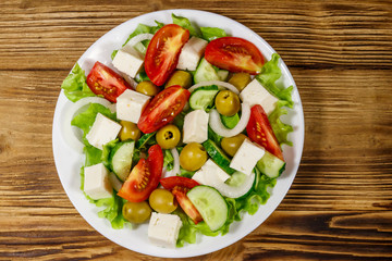 Greek salad with fresh vegetables, feta cheese and green olives on wooden table. Top view
