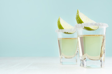 Summer fresh gold shot drinks - tequila in shot glass with lime, salt on edge on soft light pastel blue background.