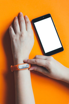 Fitness tracker on a woman hand on an orange background and mock up of smartphone.
