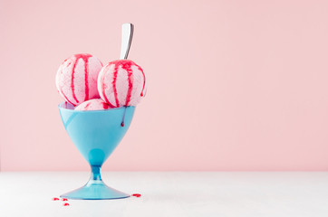 Homemade pink ice cream scoops in blue ice-cream bowl with strawberry jam, spoon in modern pink interior on white wood board.