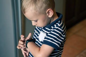 Cute little blond boy with blue eyes points out to digital fitness tracker on his wrist. Serious...
