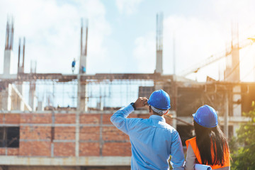 Asian man civil engineer and woman architect wearing blue safety helmet meeting at contruction site.