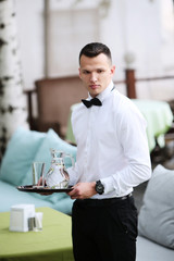 A young, handsome waiter is holding a tray in a carafe of water. The concept of the restaurant business. The staff in the field of restaurant business.