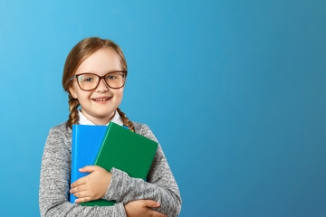 Portrait of a charming little girl schoolgirl in glasses on a blue background. The child holds...