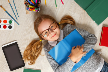 Cute little girl in glasses with a book lying on the floor. A child is surrounded by a book,...