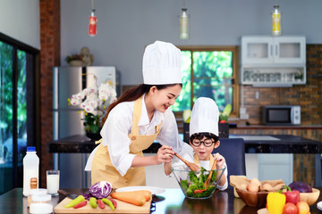 Happy asian family in the kitchen.Mother and son help to make vegetable salad.Mom teaching kid boy cooking healthy salad for dinner.