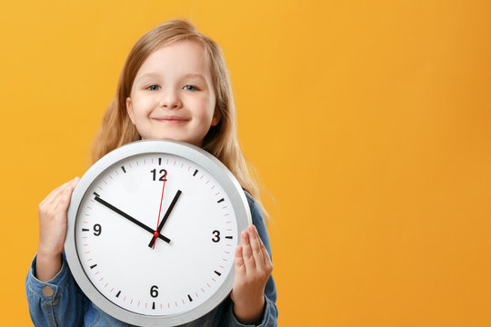A cute little girl holding a big clock over a yellow background. The concept of education, school, timing, time to learn. Copy space.