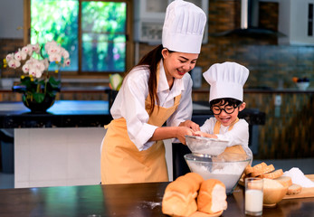 Happy asian family in the kitchen.Mother and son help to make cake.Mom teaching boy cooking bread...
