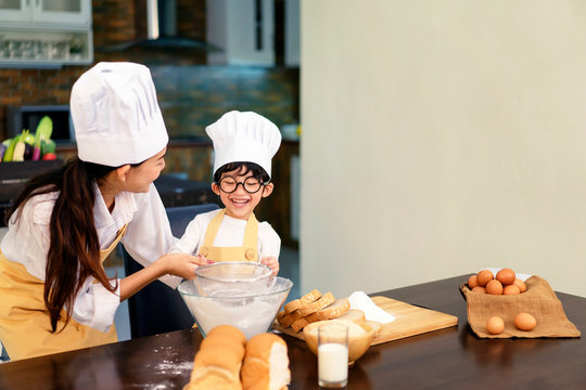 Happy Asian Family In The Kitchen.Mother And Son Help To Make Cake.Mom Teaching Boy Cooking Bread Dough.Sweet Cute Boy Is Learning How To Make A Cake In The Kitchen.