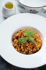 Close-up of fregola pasta with bell pepper and capers served in a white plate, studio shot