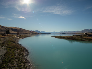 Fototapeta na wymiar View of Lake Tekapo, New Zealand, with turquoise blue water and sun flare
