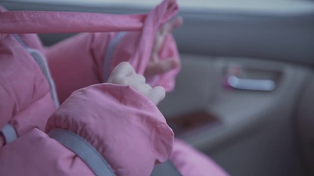 little girl in bright pink winter jacket sits in modern car salon with fastened seat belt extreme close view