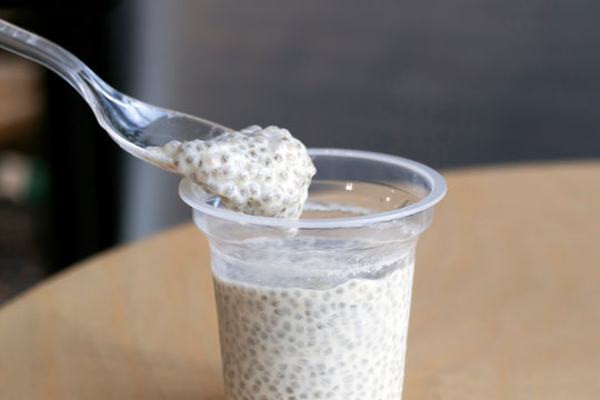 Taking spoon of chia seeds with coconut milk pudding from plastic cup on wooden table in cafe. Healthy food concept. Close-up, copy space