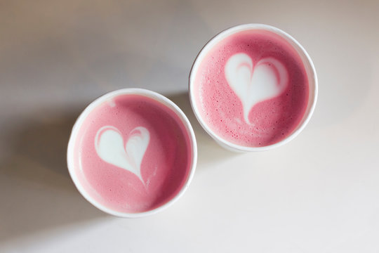 Two pink coffee cups with heart shape latte art on white table, toned. Love, Valentine's Day concept. Top view, flat lay, copy space