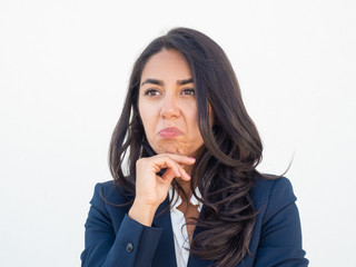 Impressed business woman feeling doubts. Young Latin woman in office suit touching chin and making skeptical, disappointed or puzzled grimace. Doubt concept