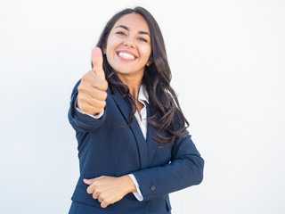Happy successful businesswoman making like gesture. Joyful beautiful young Latin woman in office suit showing thumb up and smiling at camera. Corporate support concept