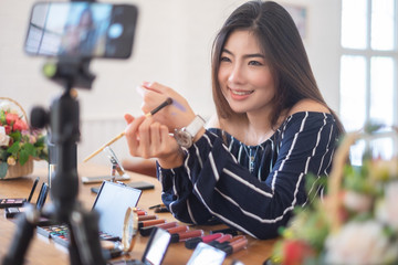 Happy girl blogger at cafe talking about makeup and beauty and recording video tutorial for...