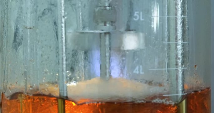The blades of the stirrer quickly spin and mix the liquid in the vessel. Experiment in the laboratory with a red liquid.